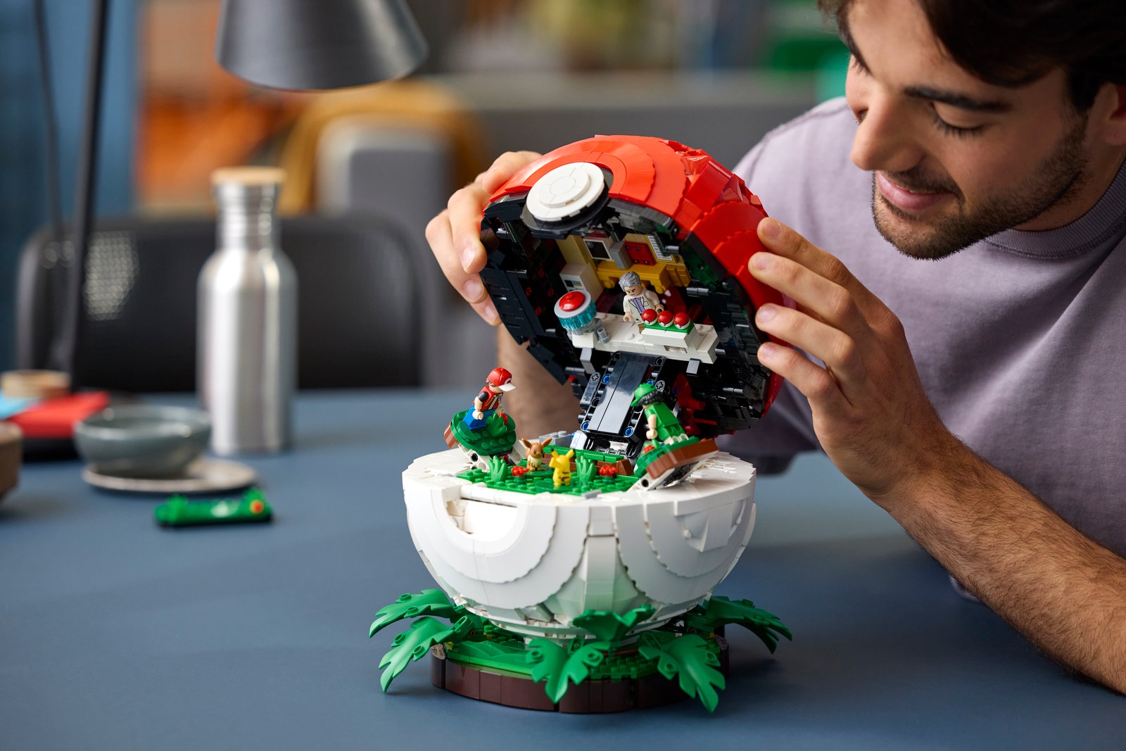 LEGO Pokémon Iconic Trainer Moments Poké Ball lifestyle image showing Professor Oak, Picnicker and Red minifigures with Pikachu and Eevee figures