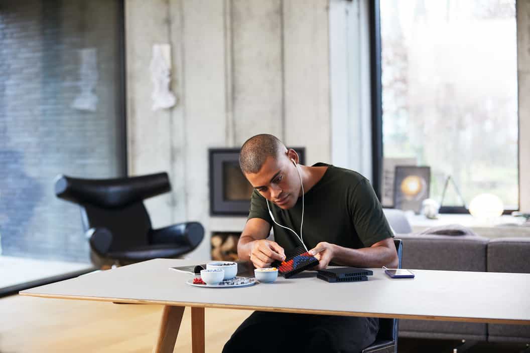 Image of a man building with LEGO tiles while listening to a soundtrack that accompanies the product