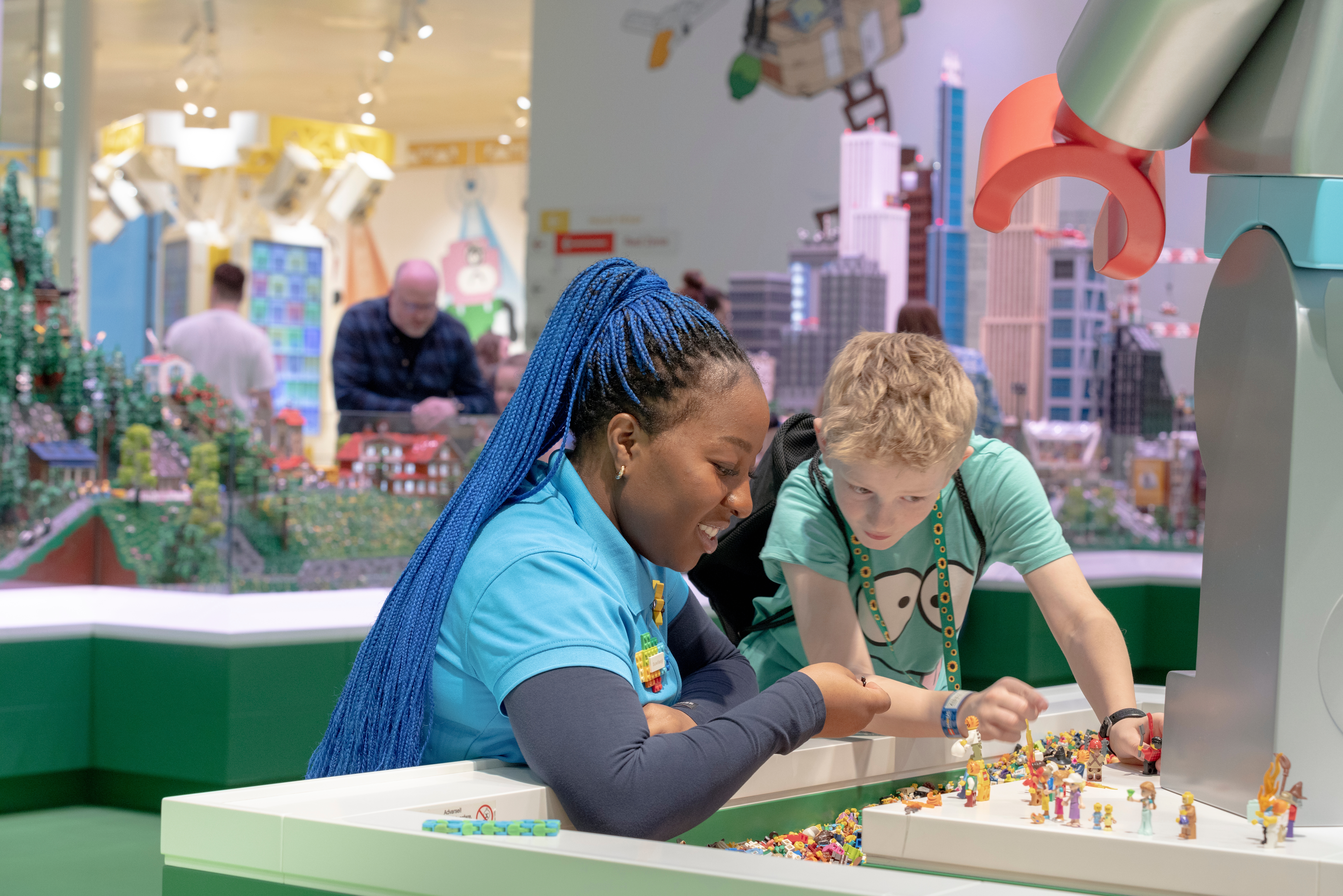 Image in LEGO House of an LEGO House employee and a child at an experience zone