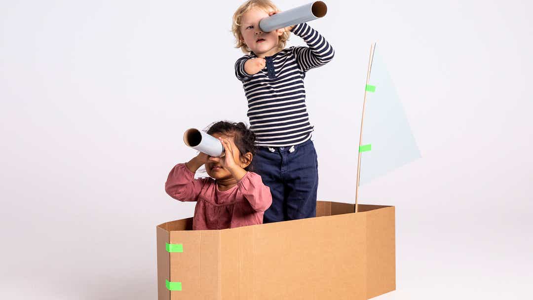 Image of girl and boy playing in a large cardboard box shaped as a boat