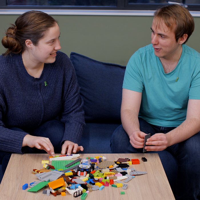 Two people talk while sat at a table of LEGO bricks