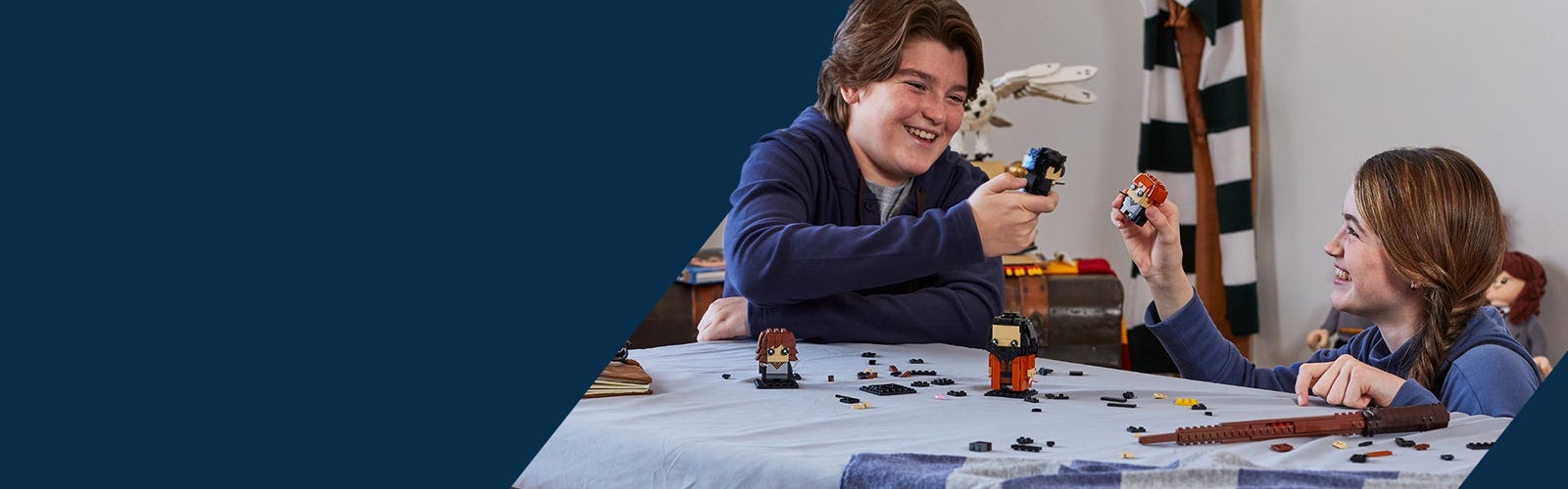 Deux enfants construisant des BrickHeadz à une table, ils tiennent dans leurs mains les personnages de Harry Potter et Ron