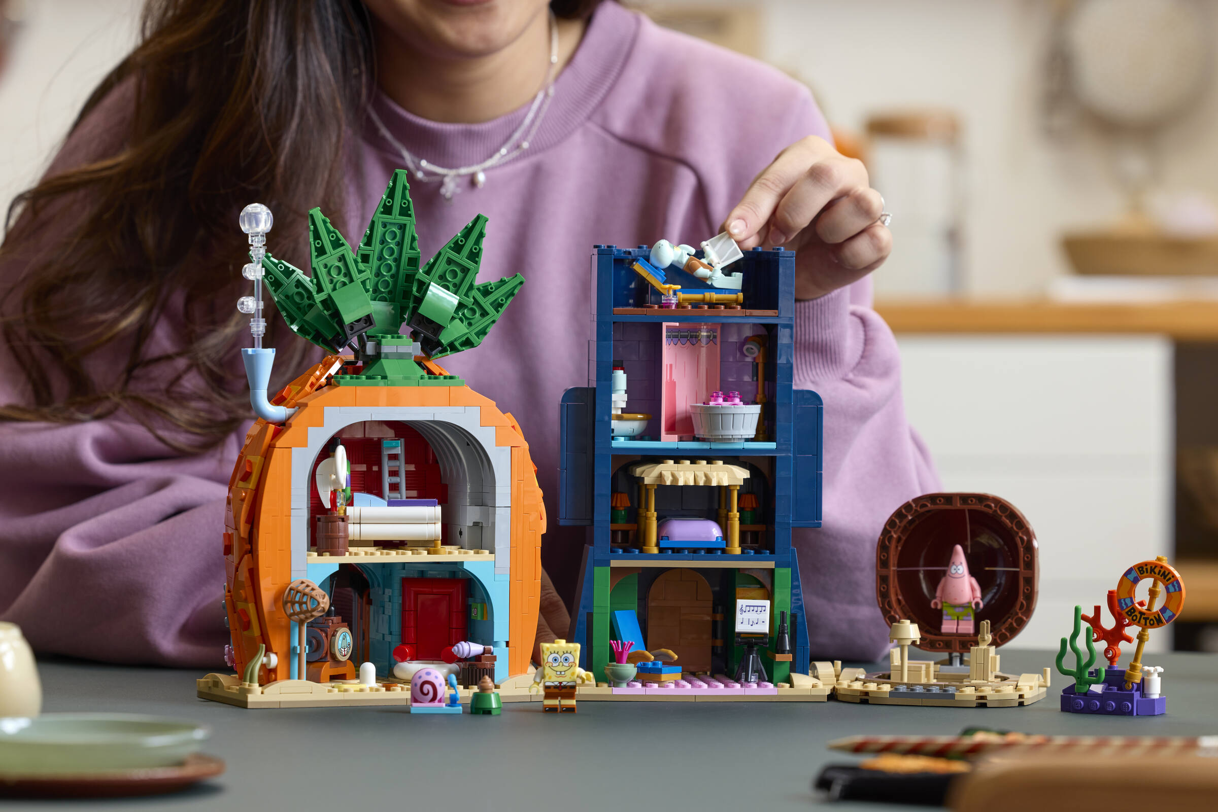 A woman placing a Squidward minifigure in his house in a LEGO® Icons SpongeBob SquarePants: Bikini Bottom set.