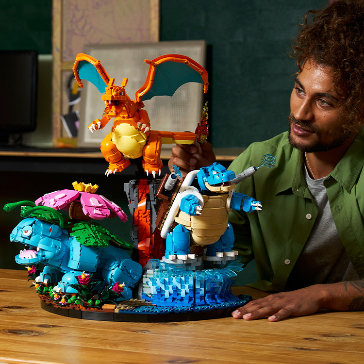 Un uomo seduto a un tavolo mentre dà gli ultimi ritocchi al set Venusaur, Charizard e Blastoise LEGO Pokémon.