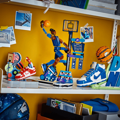 The Nike Dunk Trickshot LEGO Set on the left with the Nike Slam Dunk LEGO Set in the middle and the Nike Dunk LEGO set on the right all sitting in a row on a bookshelf.